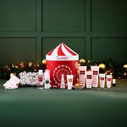 Guinot skincare products and a festive box on a green background with decorative lights.