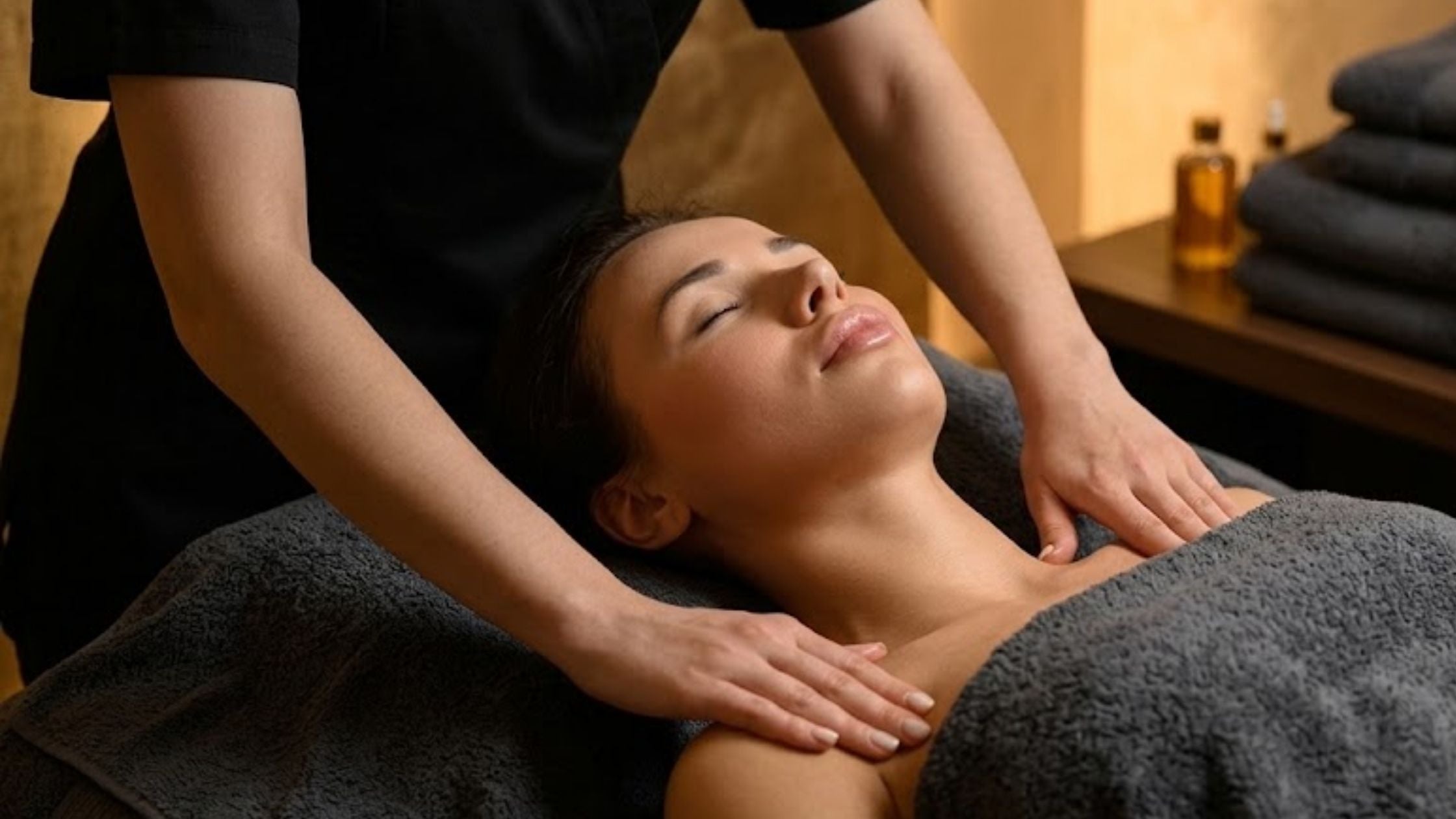 A woman laying down with her eyes closed and a therapist massaging her shoulders
