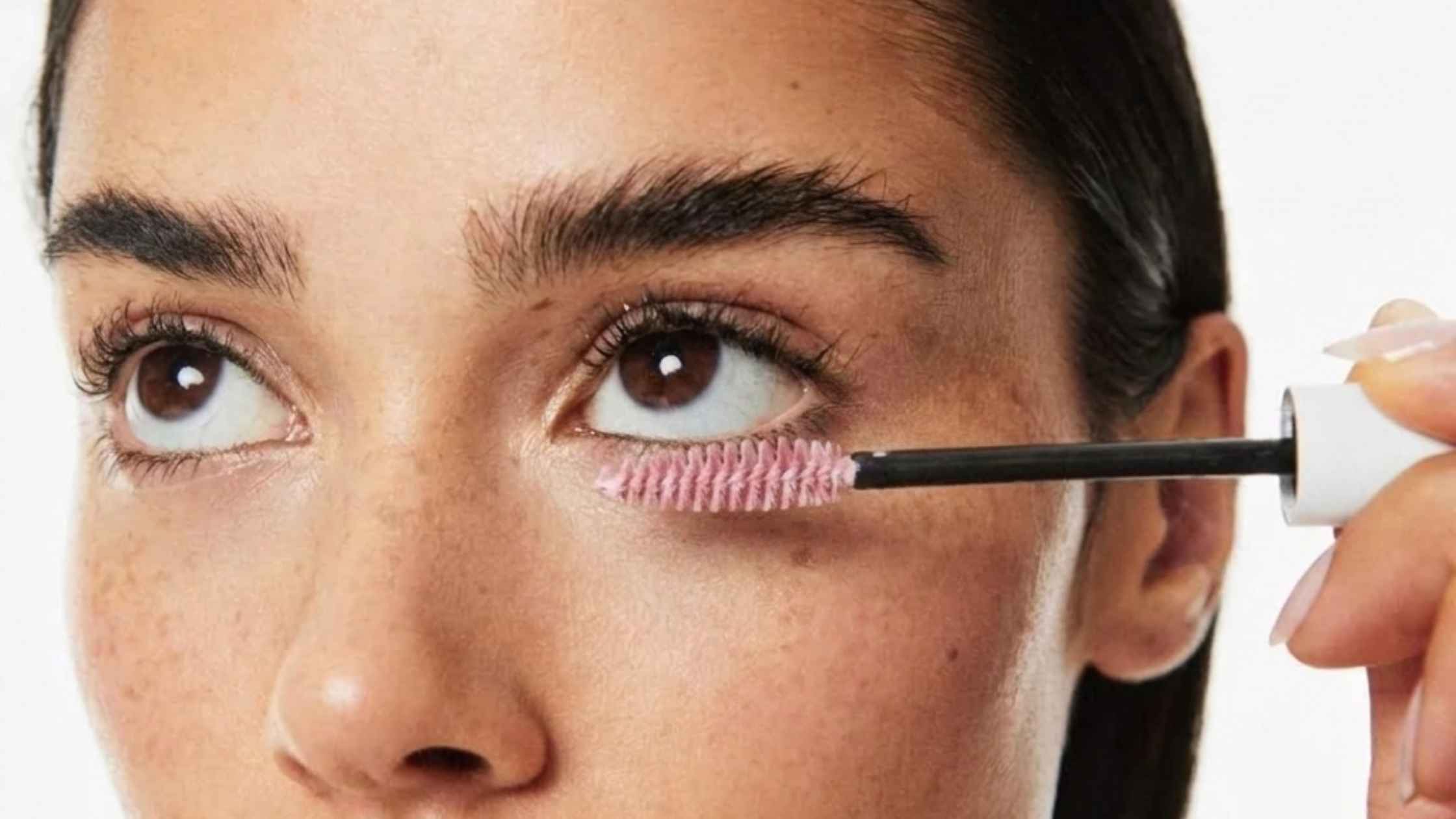 A woman looking up and combing her eyelashes with a pink brush