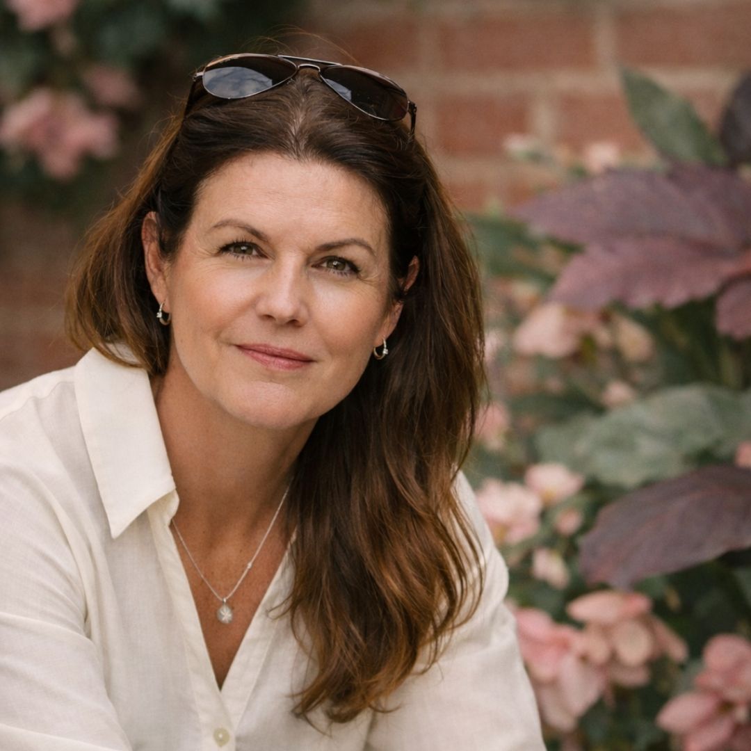 Woman with sunglasses on head, wearing a white shirt, in front of a floral background
