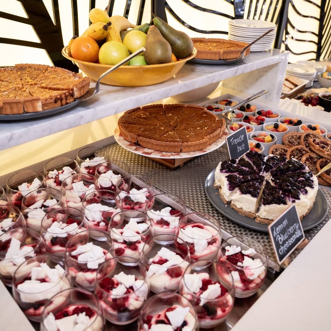 Dessert table with various pastries and fruits on a white tablecloth.