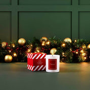 Candle and packaging with festive decorations on a green background