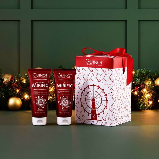 Two Guinot skincare products with a decorative box on a green background with festive decorations.