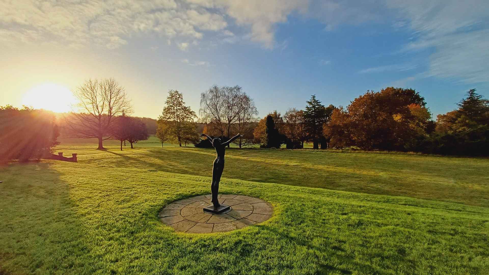 Statue of a person in a field with trees and sunset in the background