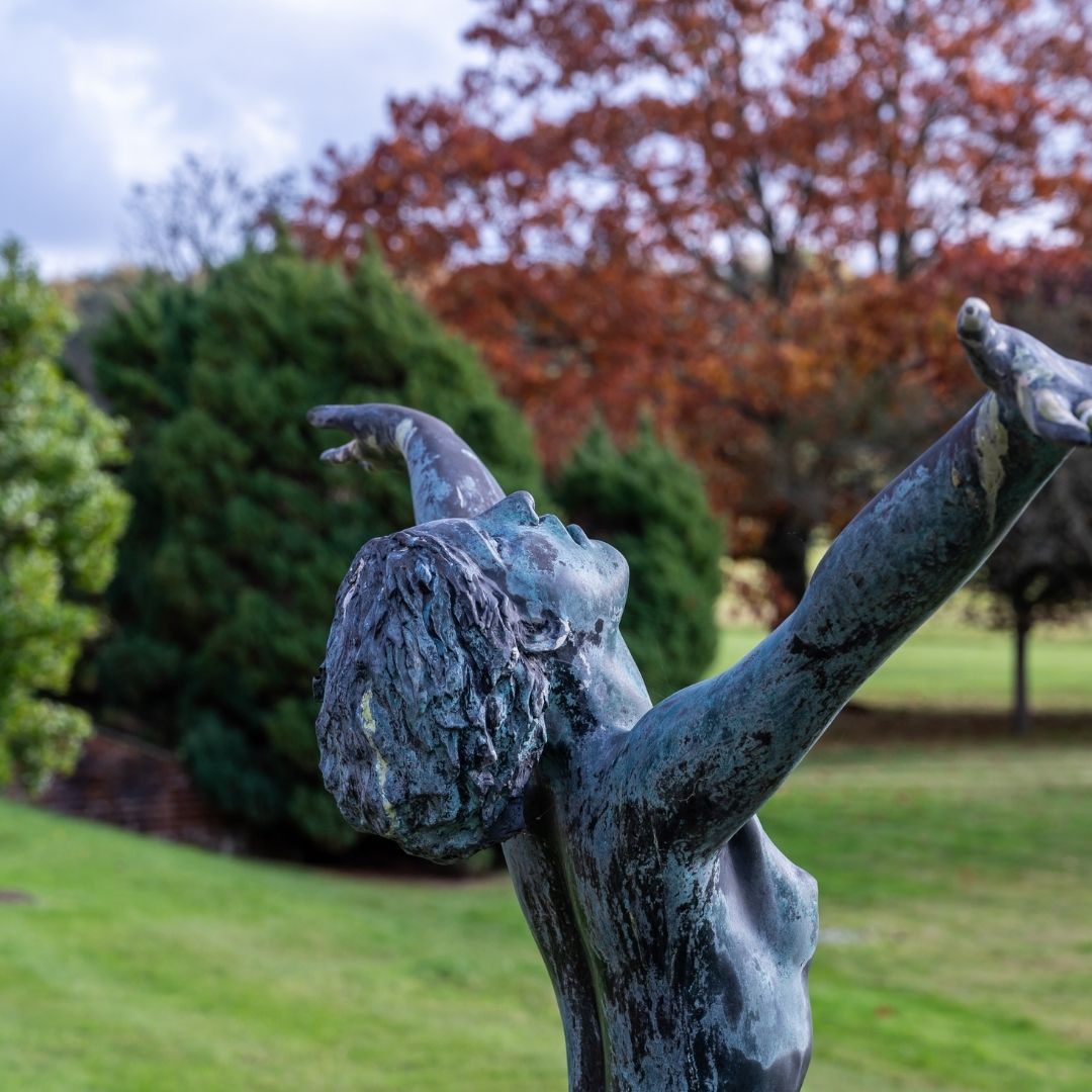 Bronze sculpture of a nude figure in a park with trees in the background