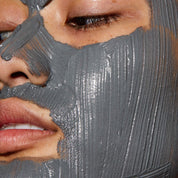 Close-up of a person applying a gray facial mask to their face.