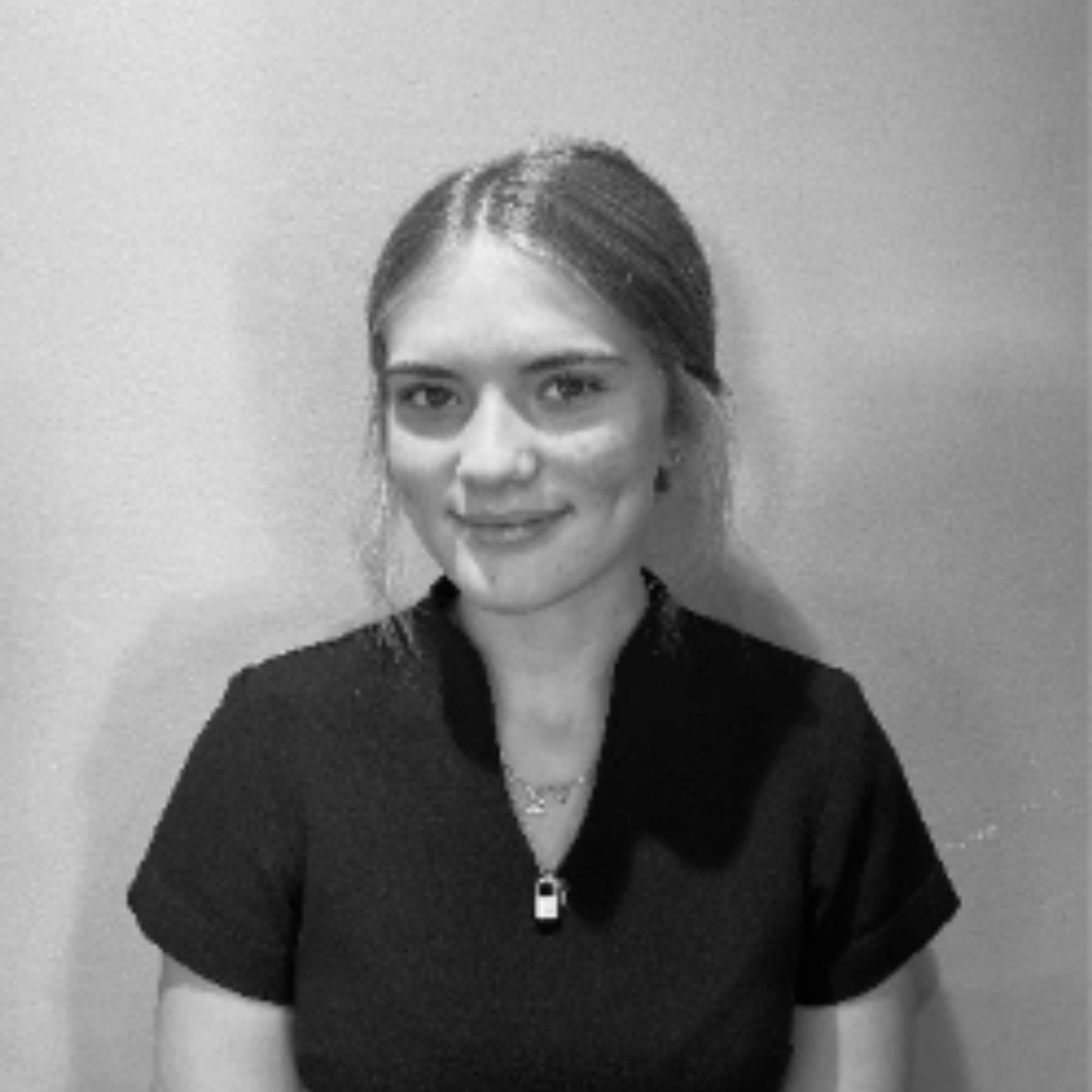 A black and white portrait of a woman with her hair pulled back, wearing a dark short-sleeve top and a small padlock pendant necklace, set against a plain light background.